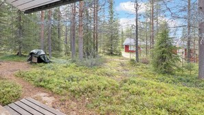 En træterrasse med udsigt over en skov, hvor en lille rød hytte ligger i det fjerne.