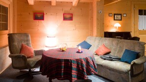 A cozy room with a wooden ceiling, a sofa, a chair, a table with a plaid tablecloth, and a lit candle. - Am Bächli by Interhome (Feutersoey)