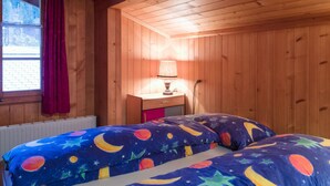 A wooden cabin room with a bed, a nightstand, a lamp, and a window with curtains. - Am Bächli by Interhome (Feutersoey)