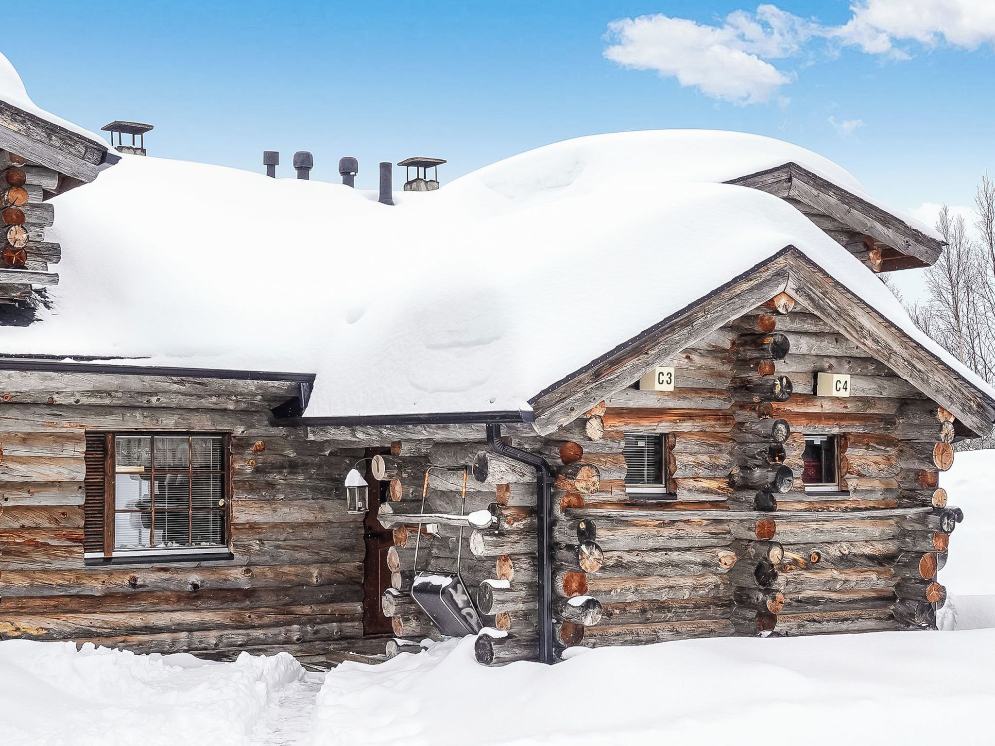 A rustic log cabin with snow-covered roofs, a chimney, and a small window with shutters.