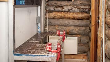 A rustic log cabin interior with a workbench, red clamps, and a white heater.