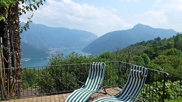 Zwei gestreifte Liegestühle auf einer gepflasterten Terrasse mit Blick auf Berge und einen See.