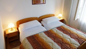 Ein Doppelbett mit einem gemusterten Quilts, zwei Nachttischlampen, ein gerahmtes Bild an der Wand und ein Fenster mit Vorhängen.