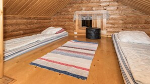 A cozy attic bedroom with wooden walls, two beds, a striped rug, and a small window with a curtain.