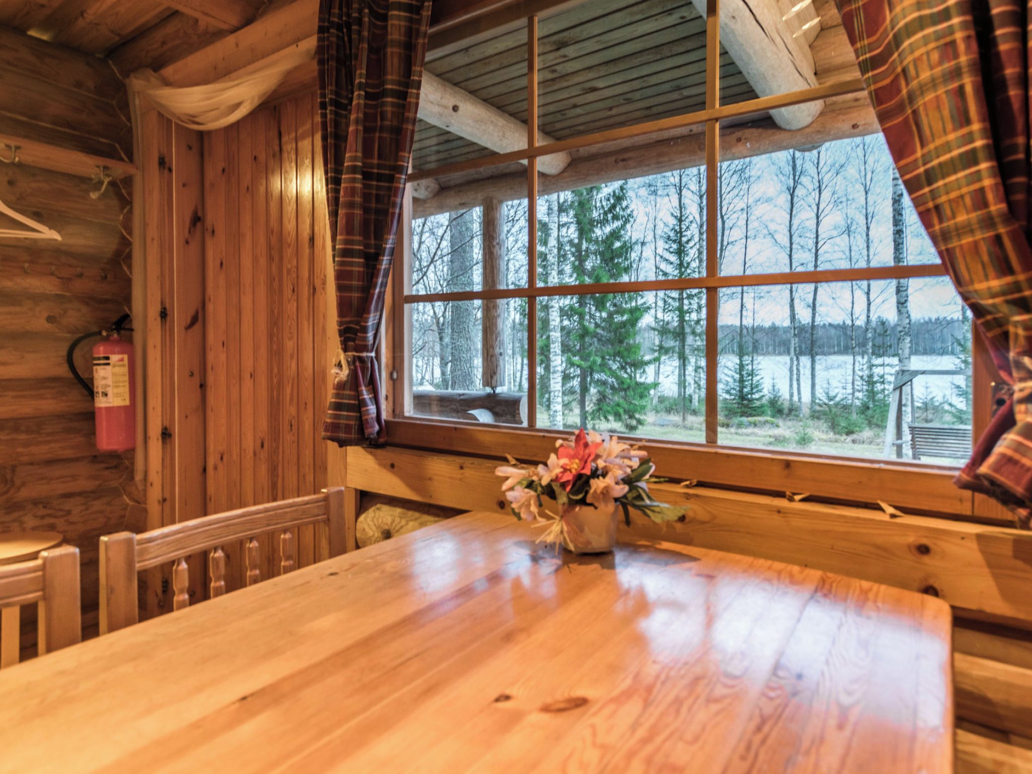 L’intérieur d’un chalet en bois, avec une grande fenêtre, une table en bois et un extincteur.
