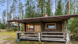A rustic log cabin with a wooden porch, a chimney, and a window.