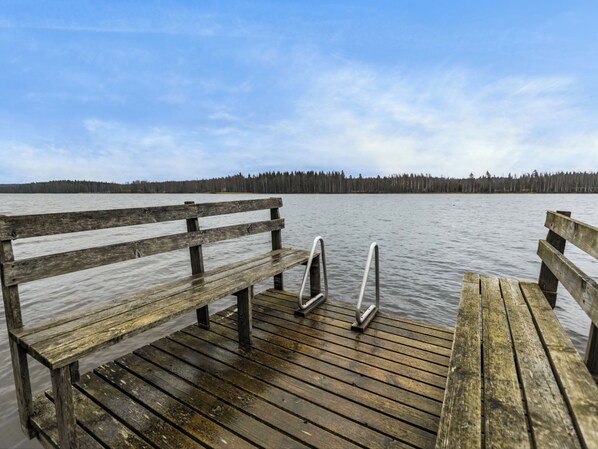 A wooden dock with benches extending over calm water, leading to a forested shoreline.