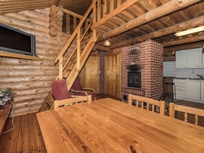 A log cabin interior with a wooden dining table, two chairs, a fireplace, and a kitchen area. - Vacation home Mikko by Interhome (Hankasalmi)
