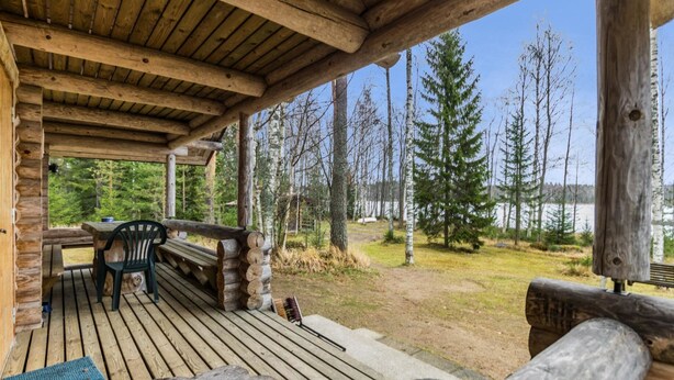 A wooden deck with a bench and table, surrounded by trees and a view of a lake.