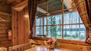 A wooden cabin interior with a large window, a wooden table, and a fire extinguisher.