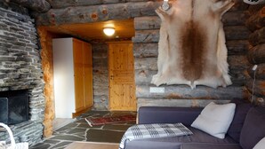 Ein Holzblockhaus-Interieur mit Kamin aus Stein, einem Lederfell an der Wand, einer Couch und einem gemusterten Teppich.