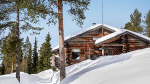 Eine Blockhütte mit schneebedecktem Dach, umgeben von Bäumen und einer verschneiten Landschaft.