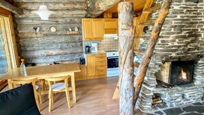 Ein rustikales Blockhaus im Inneren mit Kamin aus Stein, Holztisch und Küchenzeile.
