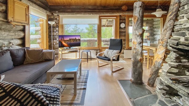 Ein rustikales Blockhaus-Interieur mit einer Couch, einem Fernseher, einem Essbereich und einer Steinsäule.