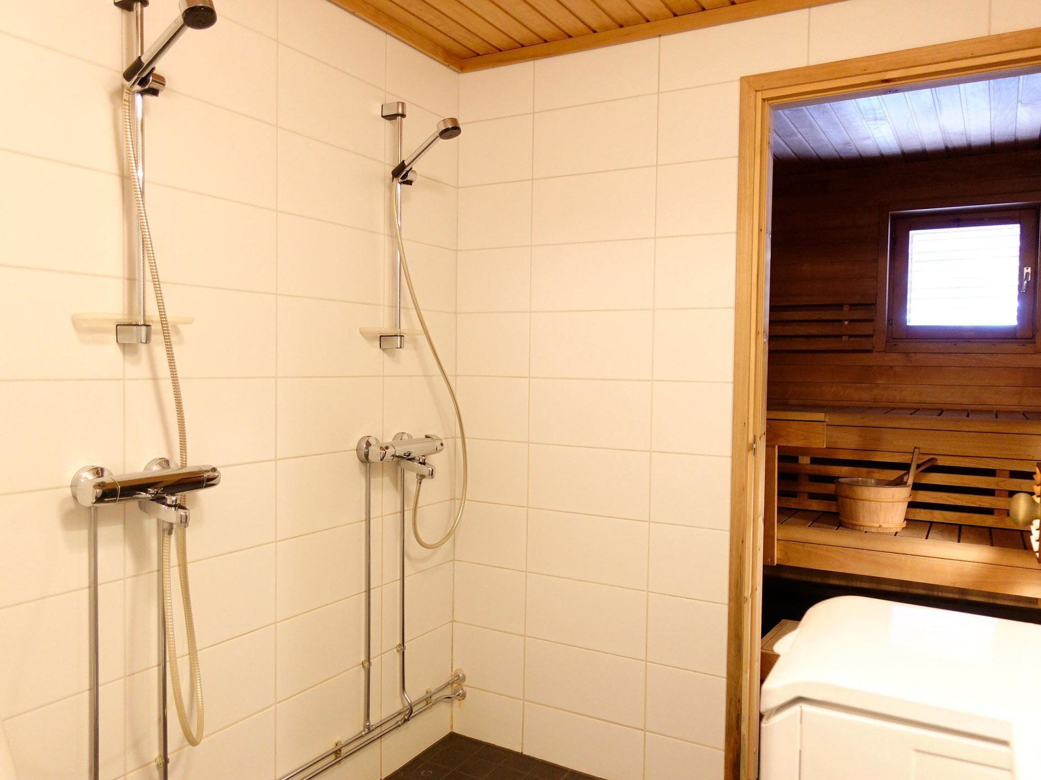 A bathroom with a shower, a toilet, and a wooden bench with a bucket and a cup.