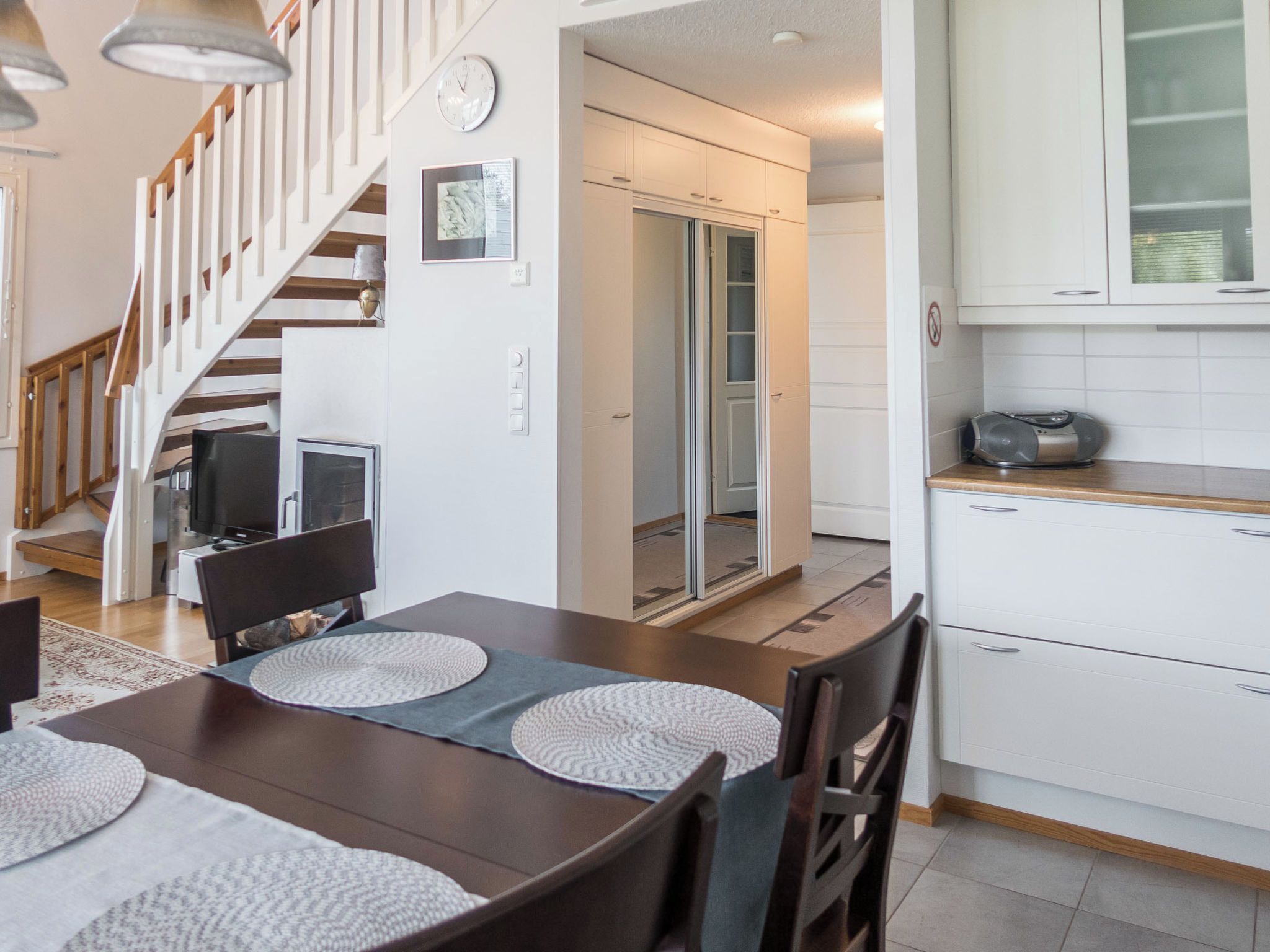 Una cocina moderna con armarios blancos, un comedor con mesa y sillas de madera, y una escalera que conduce a otro nivel.