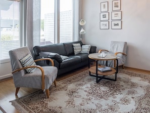 Una sala de estar moderna con un sofá de cuero, dos sillones, una mesa de centro y una alfombra estampada.