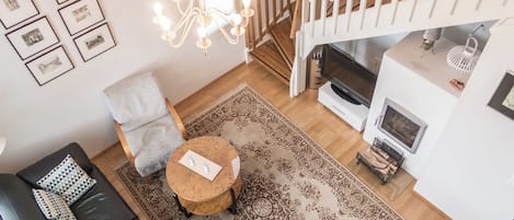 A living room with a black leather sofa, a grey armchair, a round wooden coffee table, a patterned rug, a staircase with wooden railings, and a fireplace.