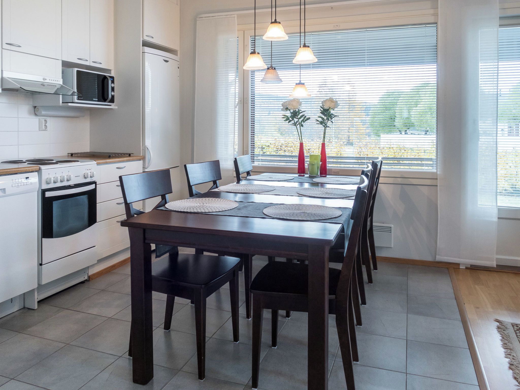 Une cuisine moderne avec des appareils électroménagers blancs, une table à manger avec des chaises et une fenêtre avec des stores.