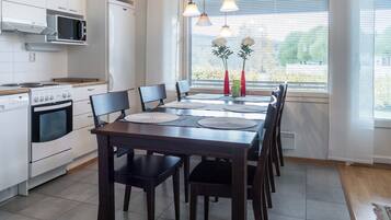 Une cuisine moderne avec des appareils électroménagers blancs, une table à manger avec des chaises et une fenêtre avec des stores.