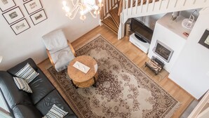 Un salon avec un canapé en cuir noir, une table basse ronde en bois, un tapis à motifs, un escalier blanc et une cheminée.