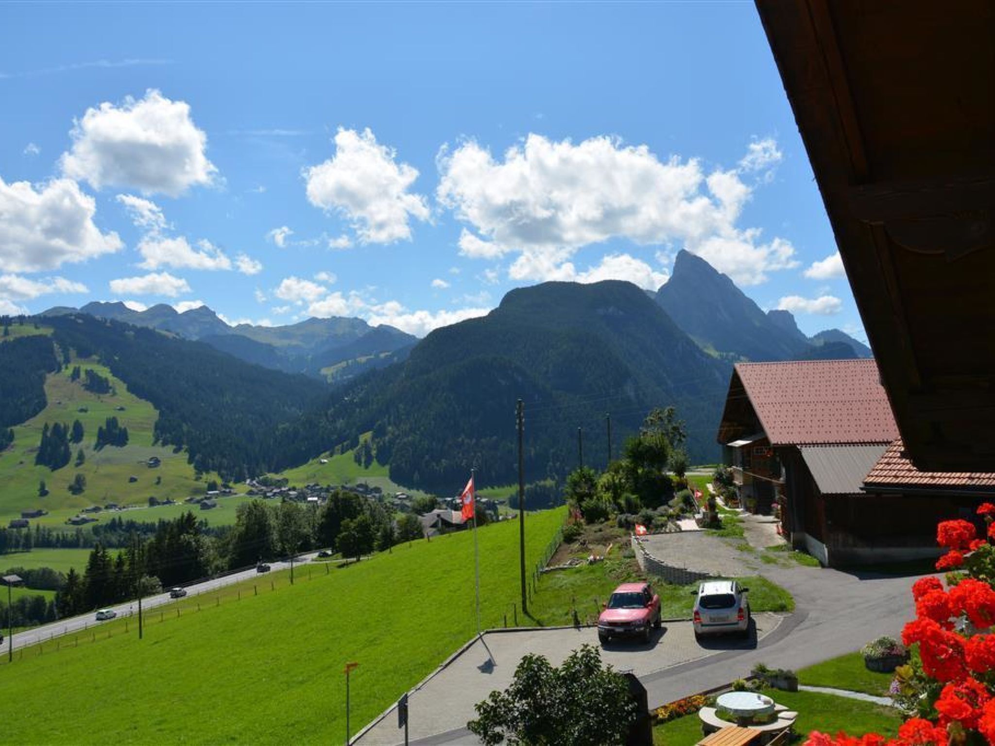 Vista de muntanya amb carretera, un edifici amb teulada vermella i una bandera.