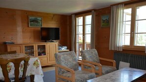 Un salon chaleureux avec un décor intérieur en bois, un téléviseur, une table à manger avec des chaises et une fenêtre avec des rideaux.