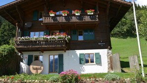 Un chalet en bois à deux étages, doté de balcons ornés de fleurs, d’un drapeau suisse et d’une enseigne indiquant « Belfort ».