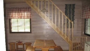 A wooden staircase with a railing, a wooden dining table with benches, and a window with blinds. - Mäntyaho by Interhome (Posio)