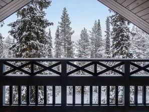 En utsikt från en balkong med ett räcke, med utsikt över ett snötäckt landskap med höga, vintergröna träd.