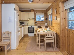 Cocina rústica de madera con una mesa de comedor, sillas, refrigerador, microondas y ventana con vistas a árboles cubiertos de nieve.