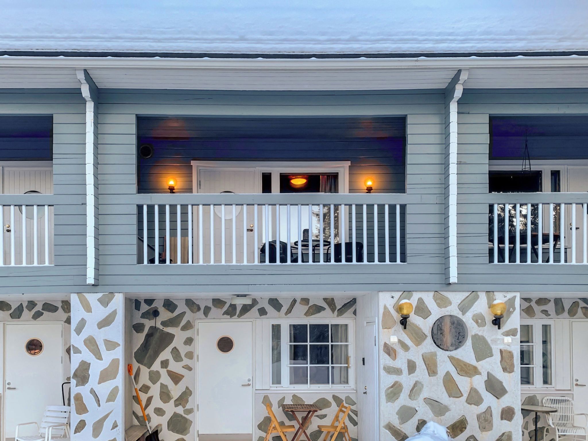 A multi-story building with a balcony, stone facade, and a small outdoor seating area.