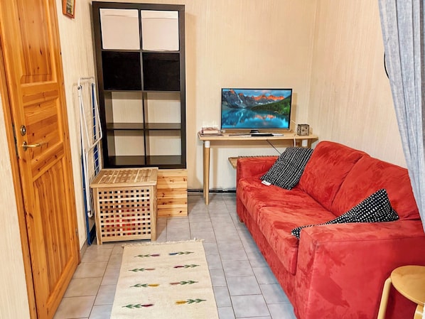 A small room with a red sofa, a wooden cabinet, a TV on a desk, and a patterned rug.