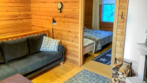 A cozy cabin with a wooden interior, a sofa, a bed with a patterned bedspread, a clock on the wall, and a window with curtains.
