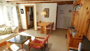 En hyggelig stue med en sofa, et spisebord med stole og et køkken, der kan anes gennem en åben dør.
