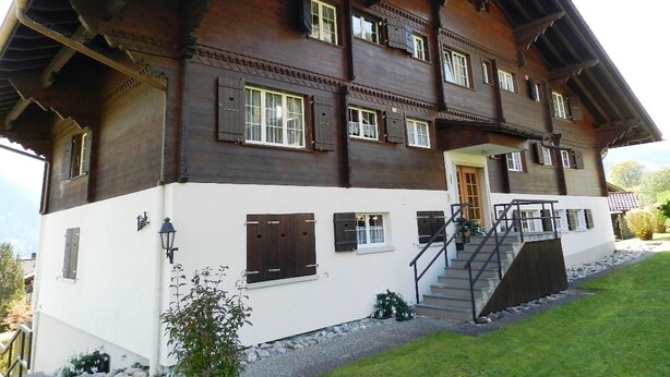 En toetages chalet med et stejlt tag, træfacade og en lille veranda med trapper op til indgangen.