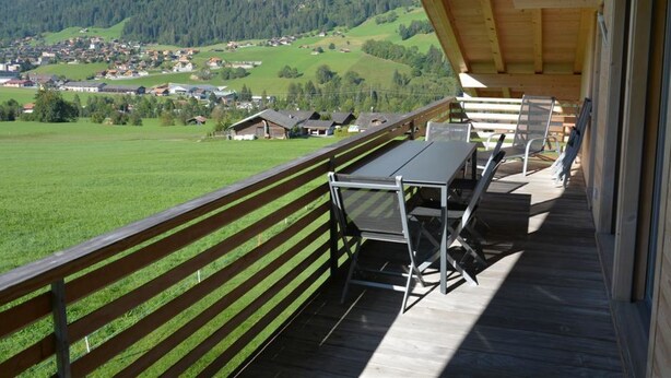 Un terrazza in legno con posti a sedere all'aperto, affacciata su una valle verde e una catena montuosa.