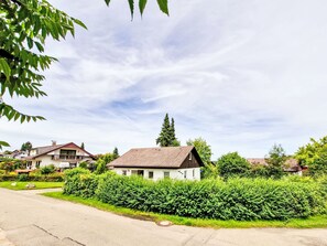 Un quartier résidentiel avec une maison blanche au toit brun, entourée d’une végétation luxuriante et d’autres maisons.