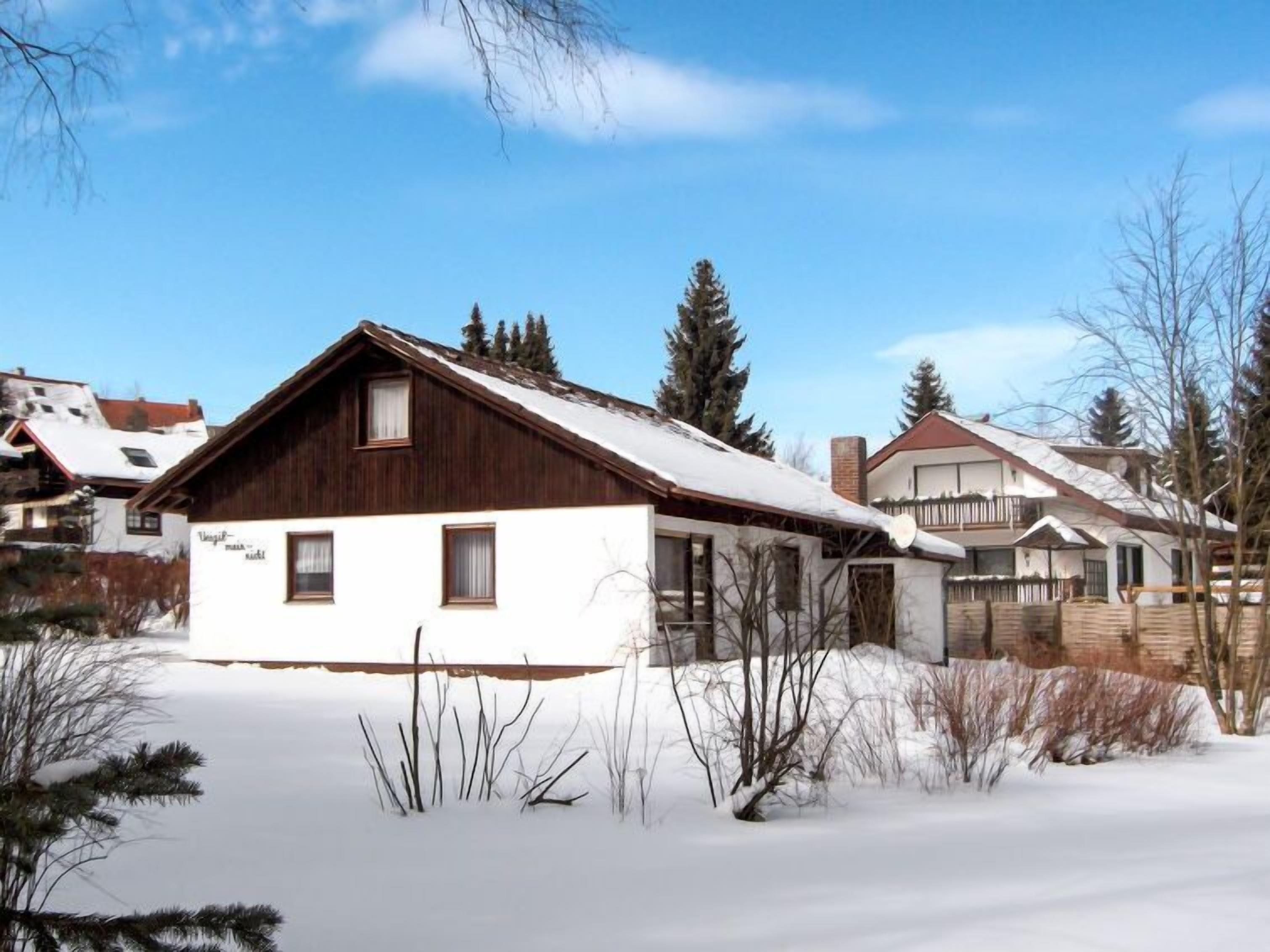 Une cabane en bois, dotée d’un toit en pente, entourée d’un paysage enneigé et d’une végétation clairsemée.