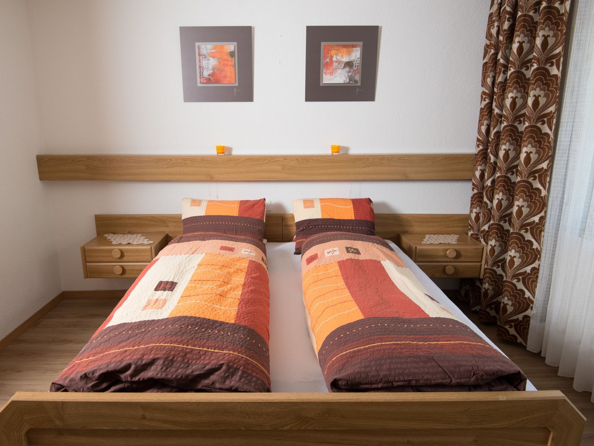 Un lit double avec une couette, une tête de lit en bois, des tables de chevet et deux tableaux encadrés au mur.