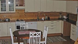 A compact kitchen with white cabinets, a stove, a sink, and a dining area with a table and chairs. - Mustikka by Interhome (Lohja)