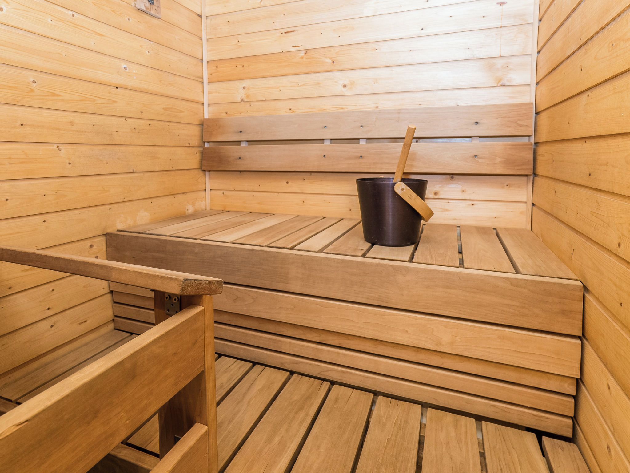 A sauna with wooden benches and a black bucket with a wooden handle.