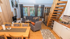 Una sala de estar acogedora con un sofá, una mesa de comedor y sillas, una cocina con un fregadero, y una escalera.