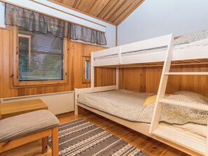 Une chambre avec un lit superposé, un plancher en bois, une fenêtre avec des stores, une petite table et un banc.