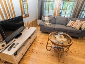 A living room with a flat-screen TV, a sofa, a wicker chair, and a glass coffee table.