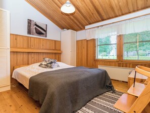 A bedroom with a wooden ceiling, a bed with a patterned pillow, a window with blinds, and a chair.