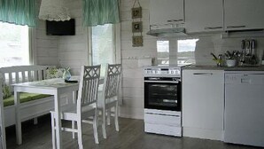 A kitchen with white cabinetry, a dining table with chairs, and a window with curtains. - Mariantupa by Interhome (Muurame)