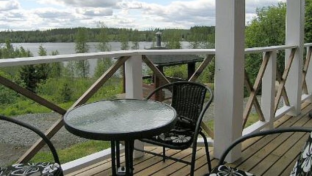 A wooden deck with a glass table and chairs, overlooking a lake and forest. - Mariantupa by Interhome (Muurame)