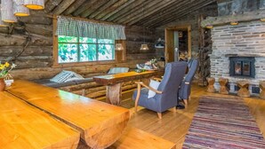 Ein rustikales Blockhaus-Interieur mit einem Holzesstisch, Bänken und Stühlen. Im Hintergrund ist ein Kamin aus Stein zu sehen.