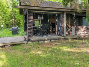 A rustic cabin with a porch, a table, and chairs.